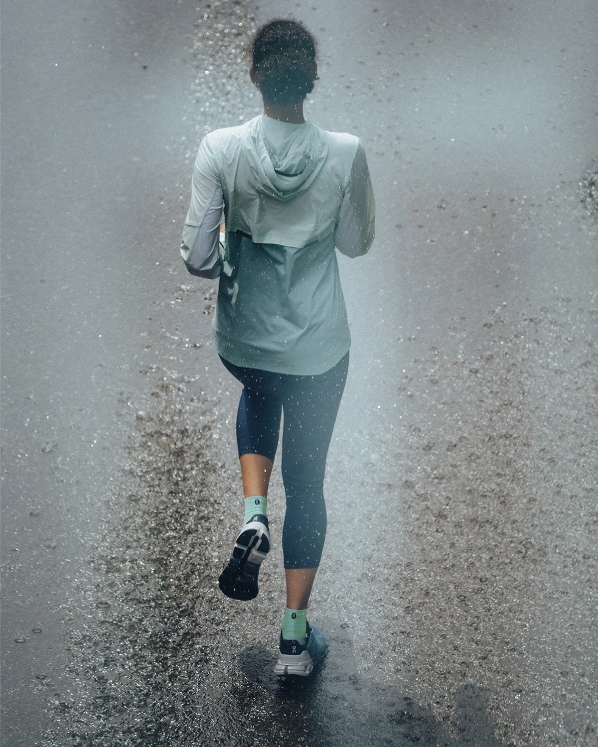 Gros plan sur une femme de dos qui descend la route en courant et porte la veste weather jacket et les leggings active tights.