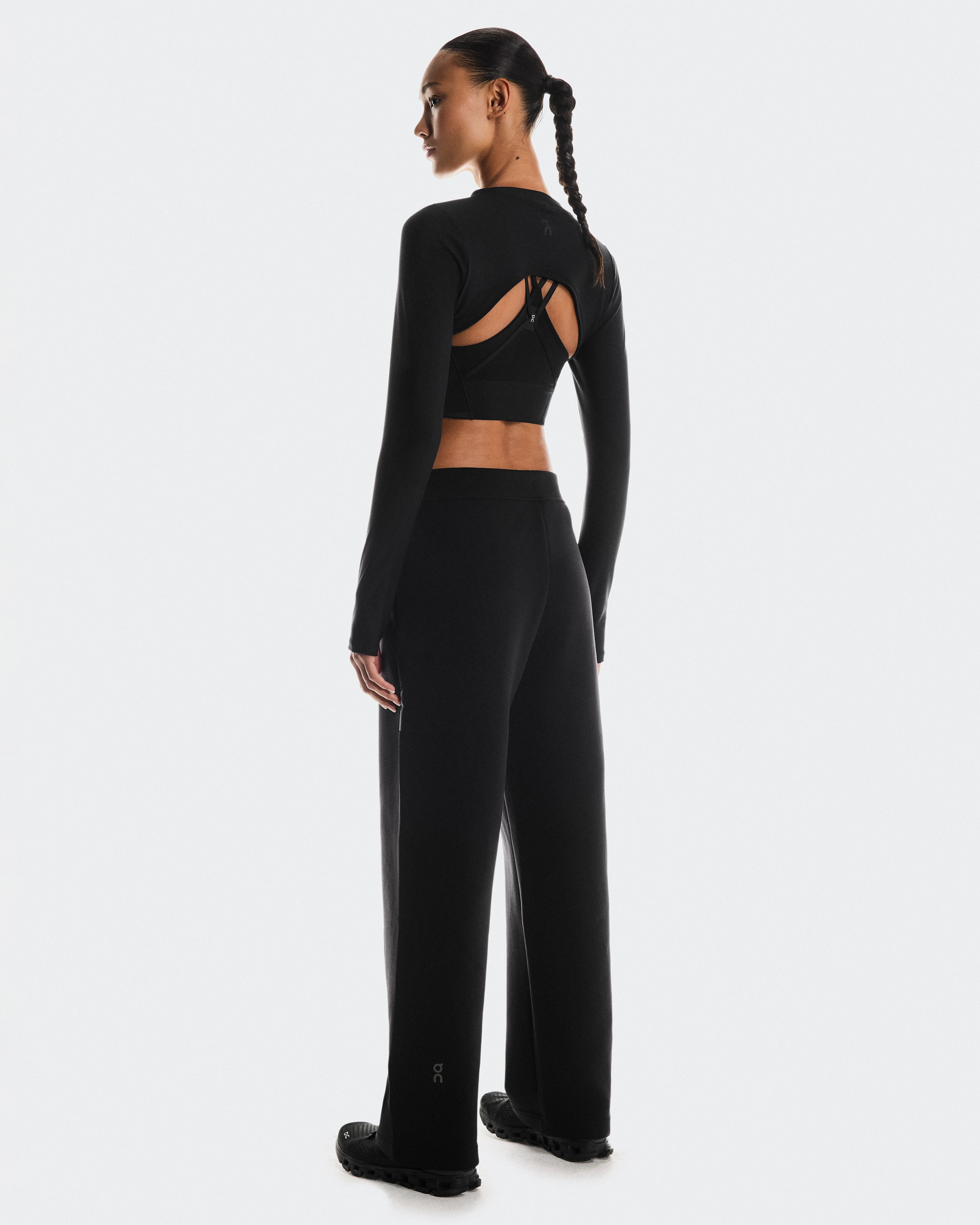 Une femme debout, de dos, entièrement vêtue de noir, portant des vêtements de sport.