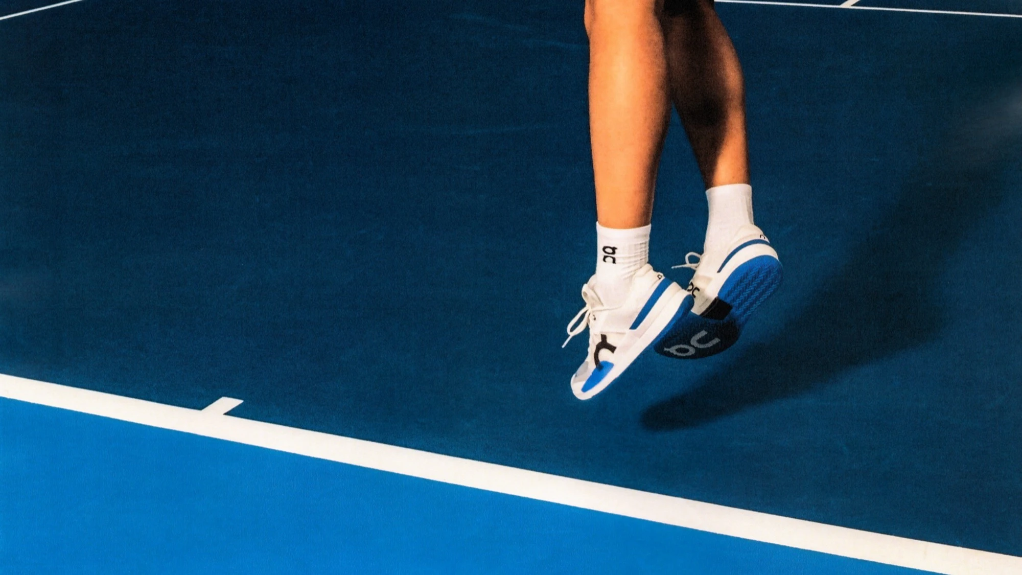 Une personne saute près de la ligne de fond d'un court de tennis bleu.