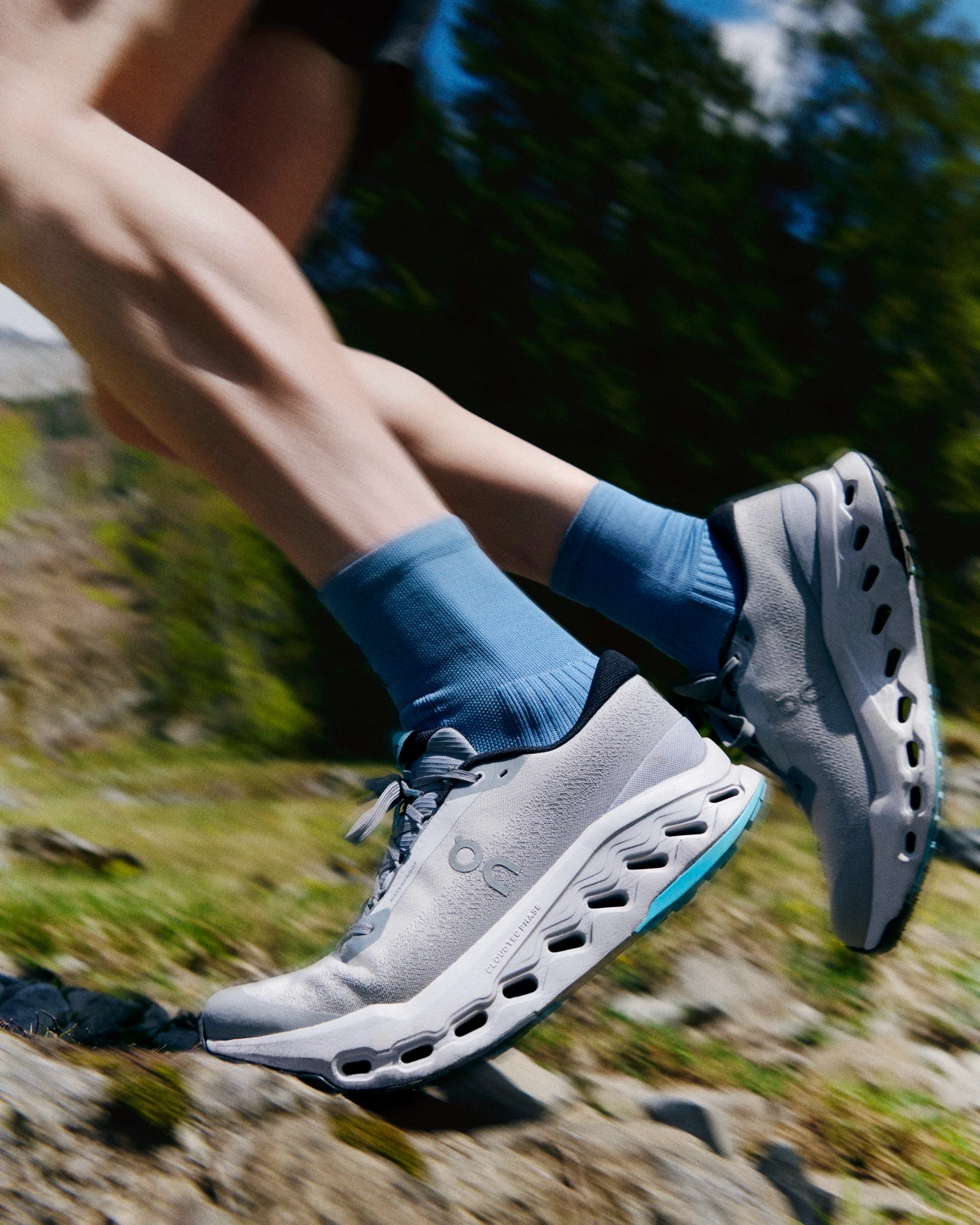 Gros plan sur des chaussures de running On sur un sentier de montagne.