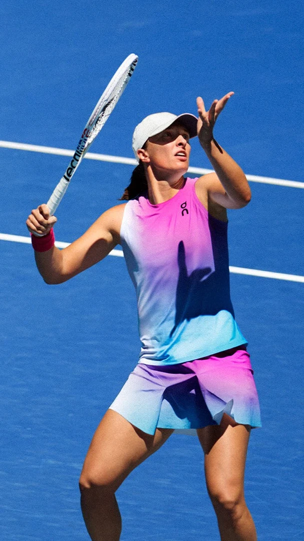 Iga Świątek dans une tenue On multicolore, prête à servir avec une balle de tennis.