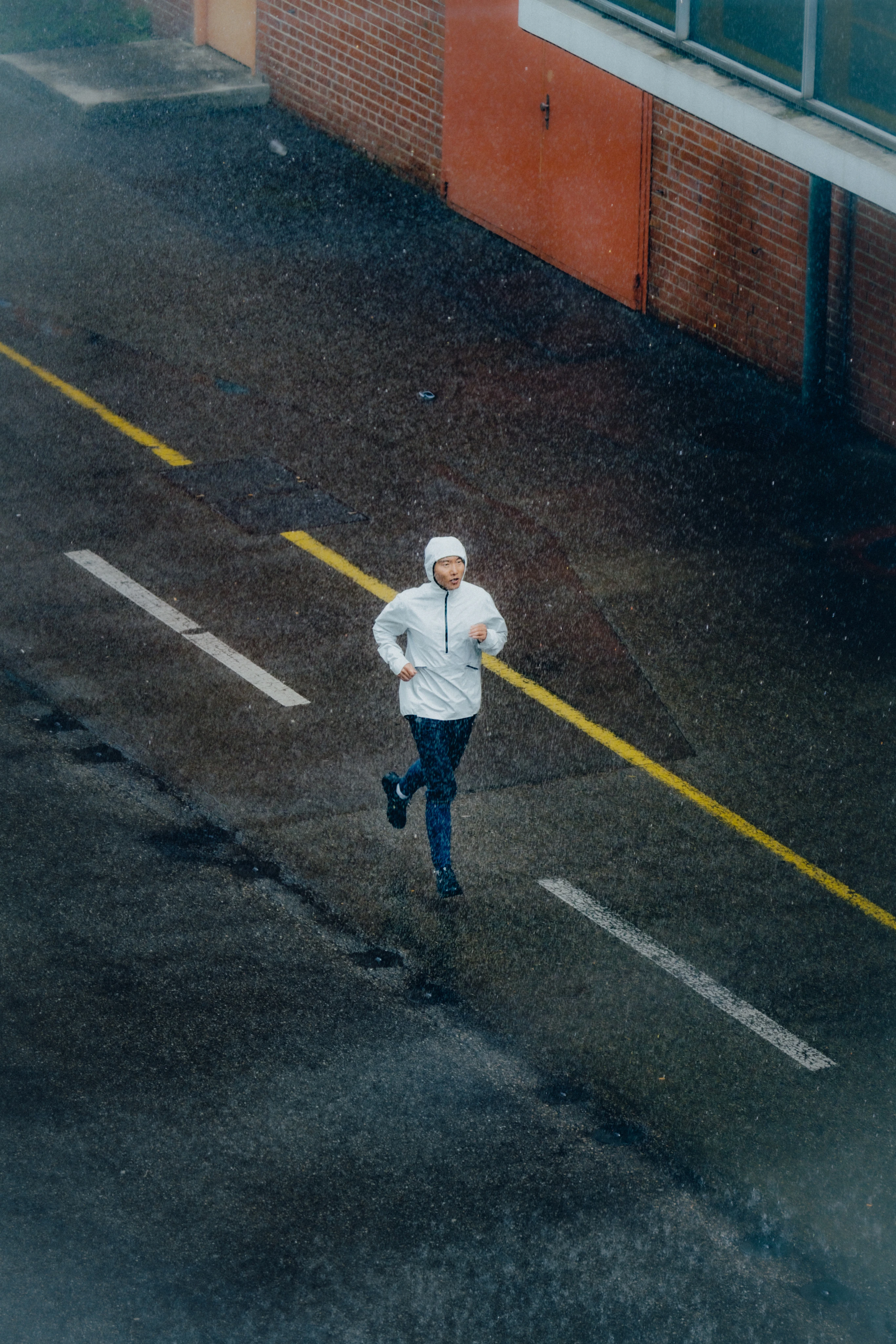 Une femme descend une route en courant sous la pluie et porte la veste waterproof anorak avec la capuche.