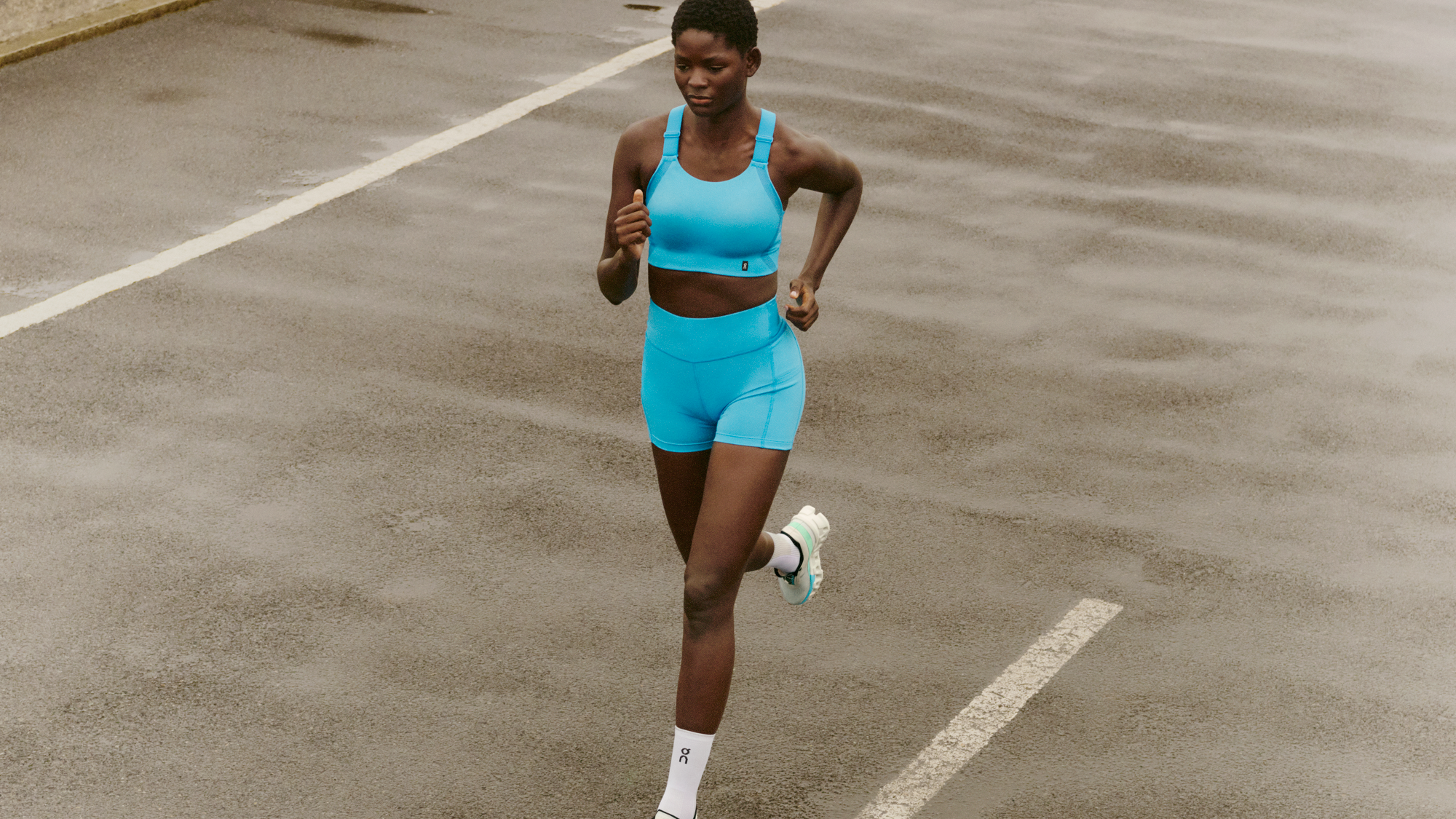Une sportive court sur une piste en soutien-gorge de sport et short bleu clair. 