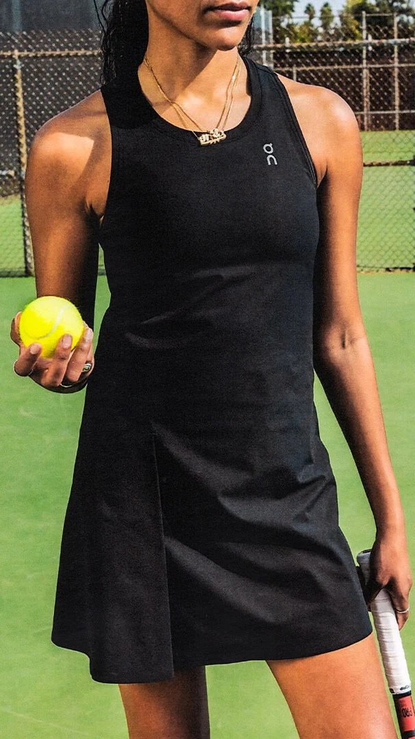 Une femme qui porte une courte robe noire, avec une raquette et une balle de tennis dans la main.