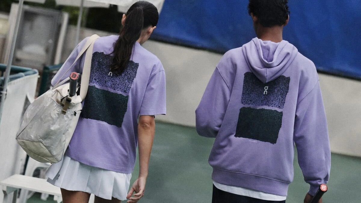 Deux joueur·ses de tennis s’éloignant du court, tous deux vêtus de hauts violets de la marque On&nbsp;: un t-shirt et un sweat-shirt.