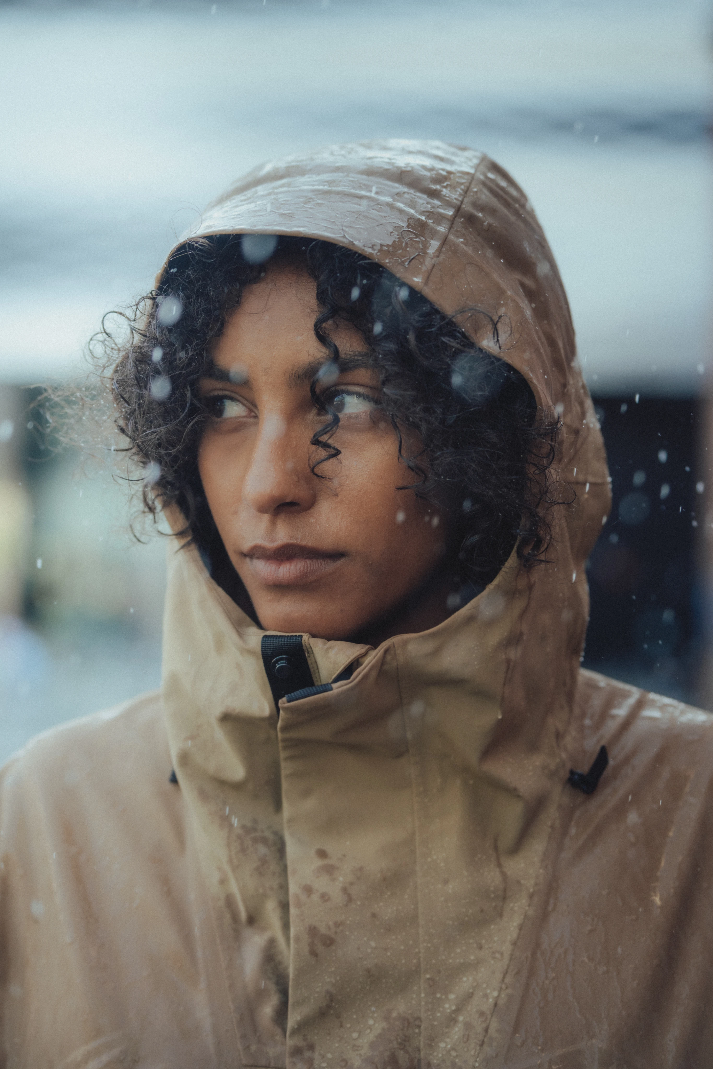 Gros plan sur une personne qui porte la veste Waterproof Jacket avec la capuche et regarde sur les côtés tandis que la pluie tombe.