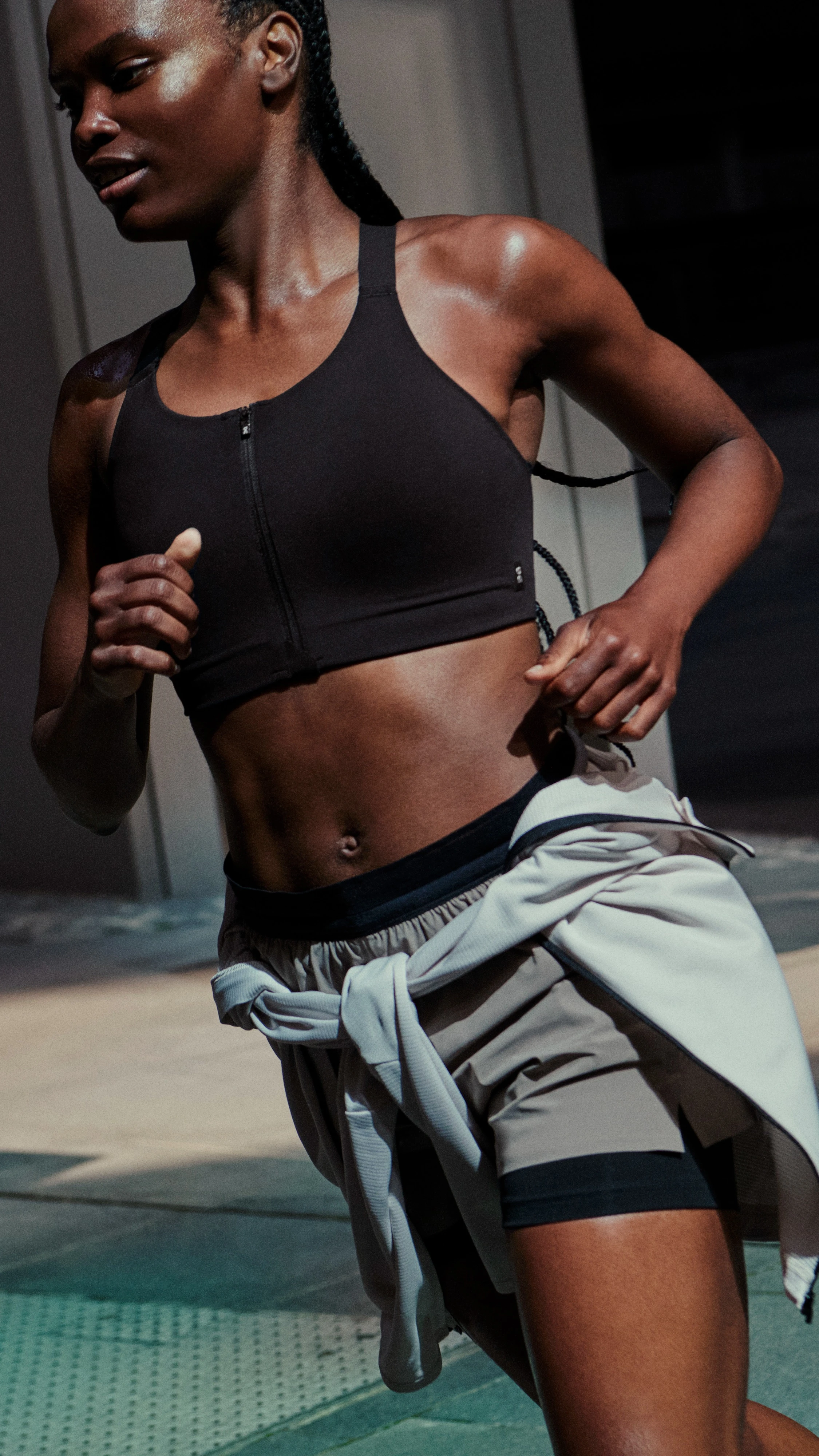Femme courant en brassière de sport et short, un pull noué à la taille.