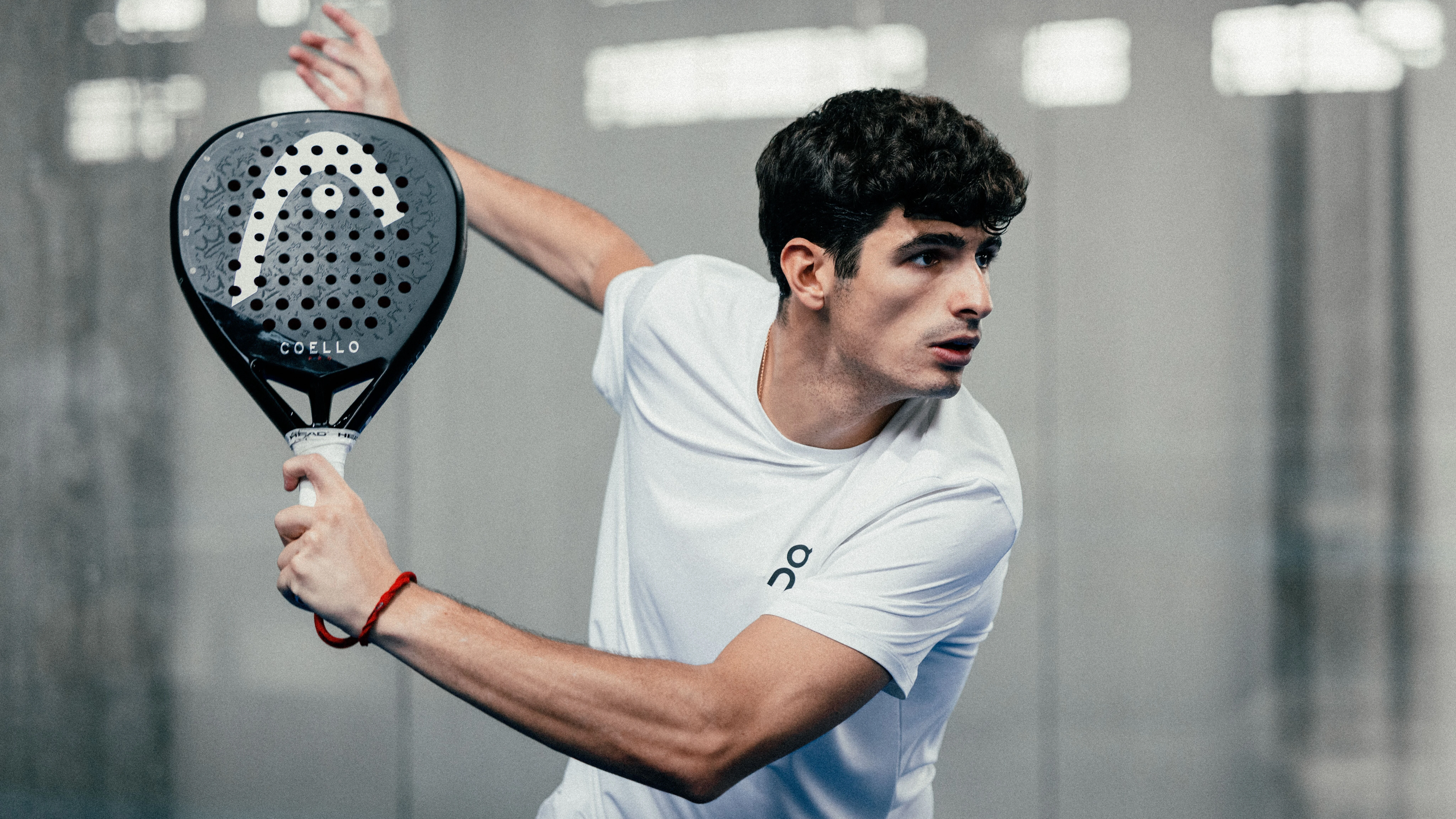 Un joueur de padel équipé de vêtements On, prêt à réagir, raquette en main.