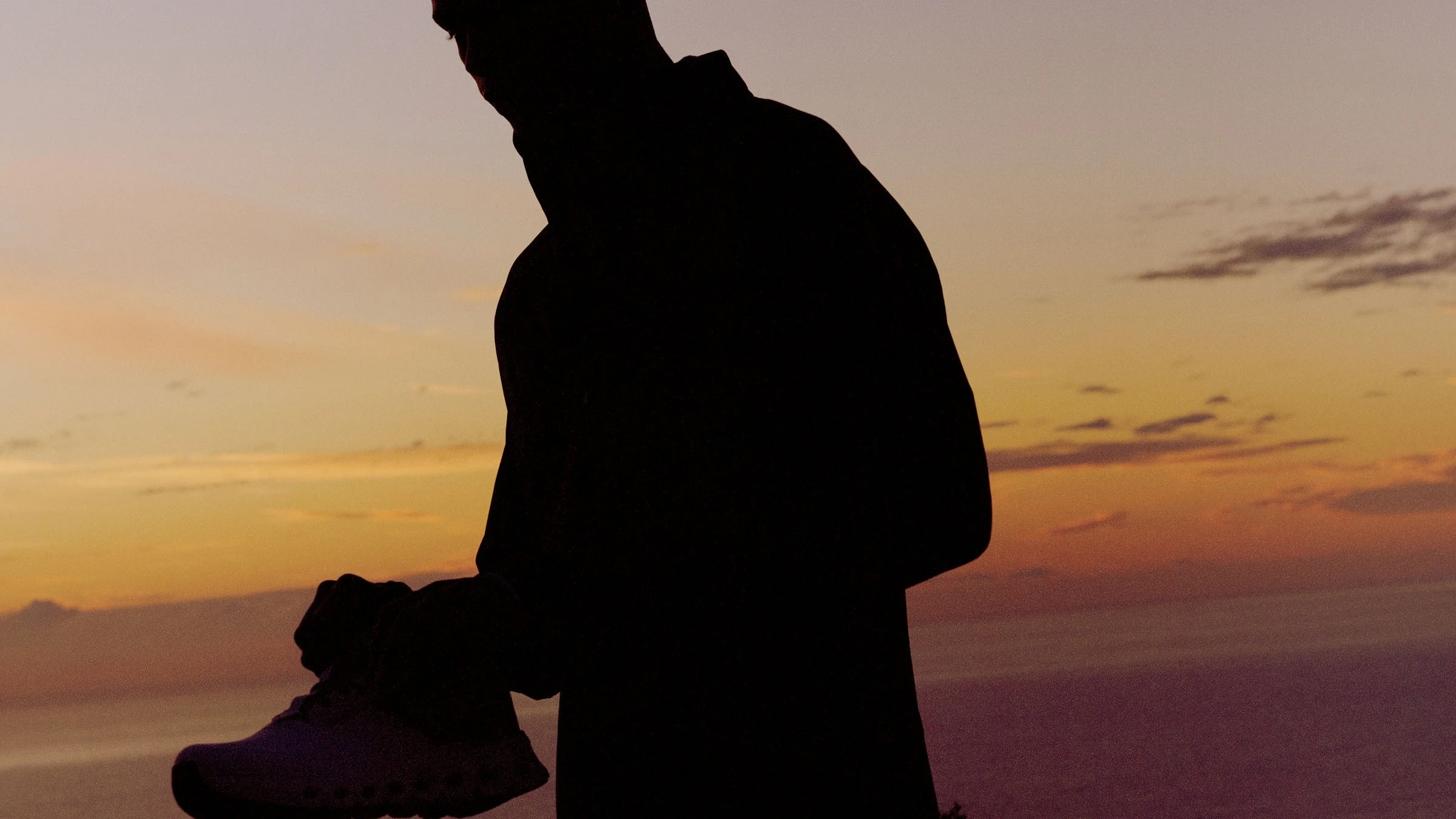Homme enfilant ses chaussures pour courir au coucher du soleil.