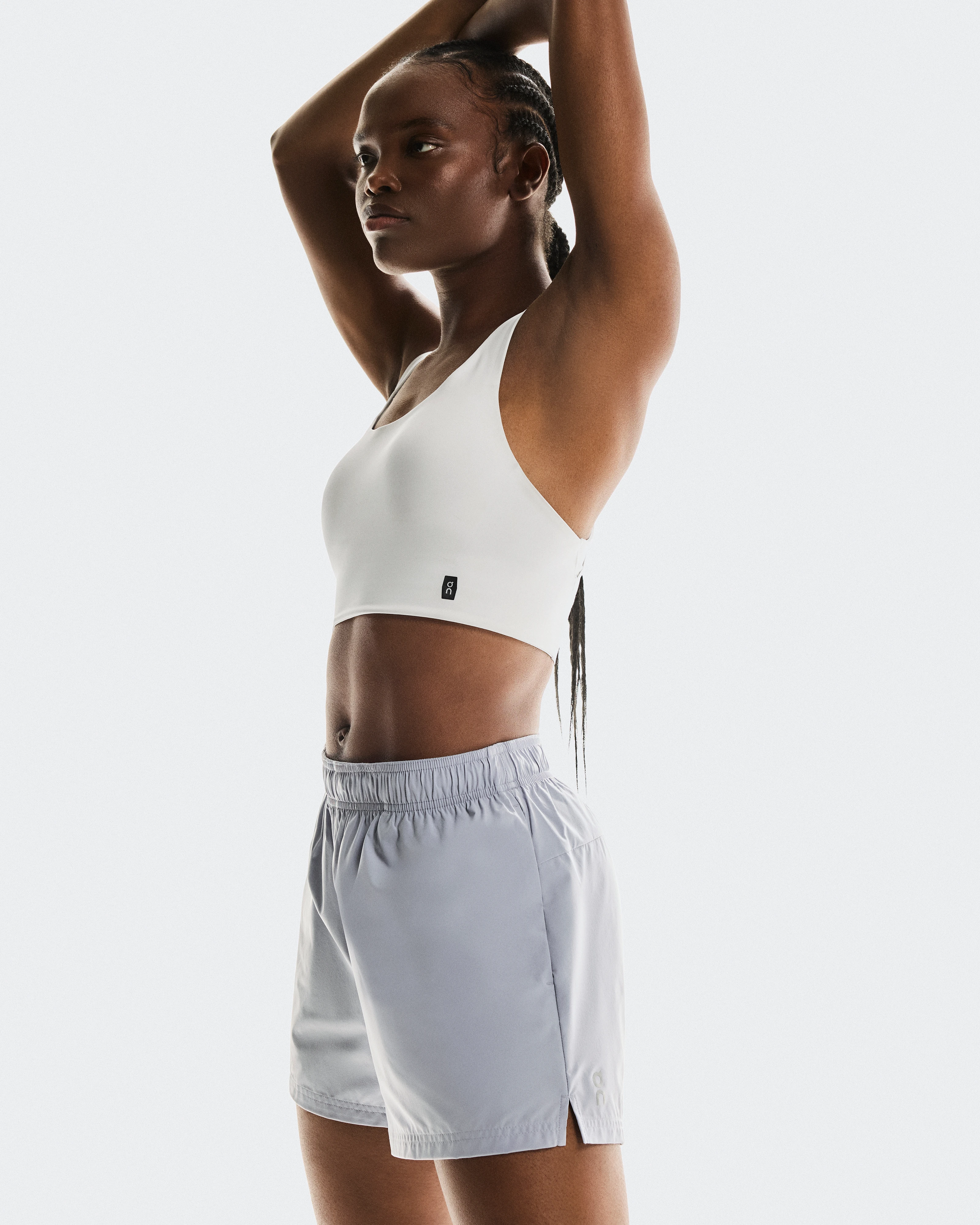 Une athlète s’étirant les épaules, vêtue d’une brassière de sport et d'un short de running On blancs.