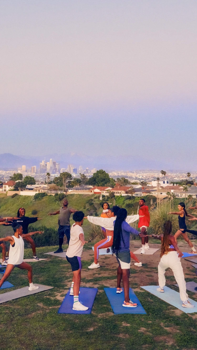 A group of people doing yoga poses on a hilltop, with a city in the distance.