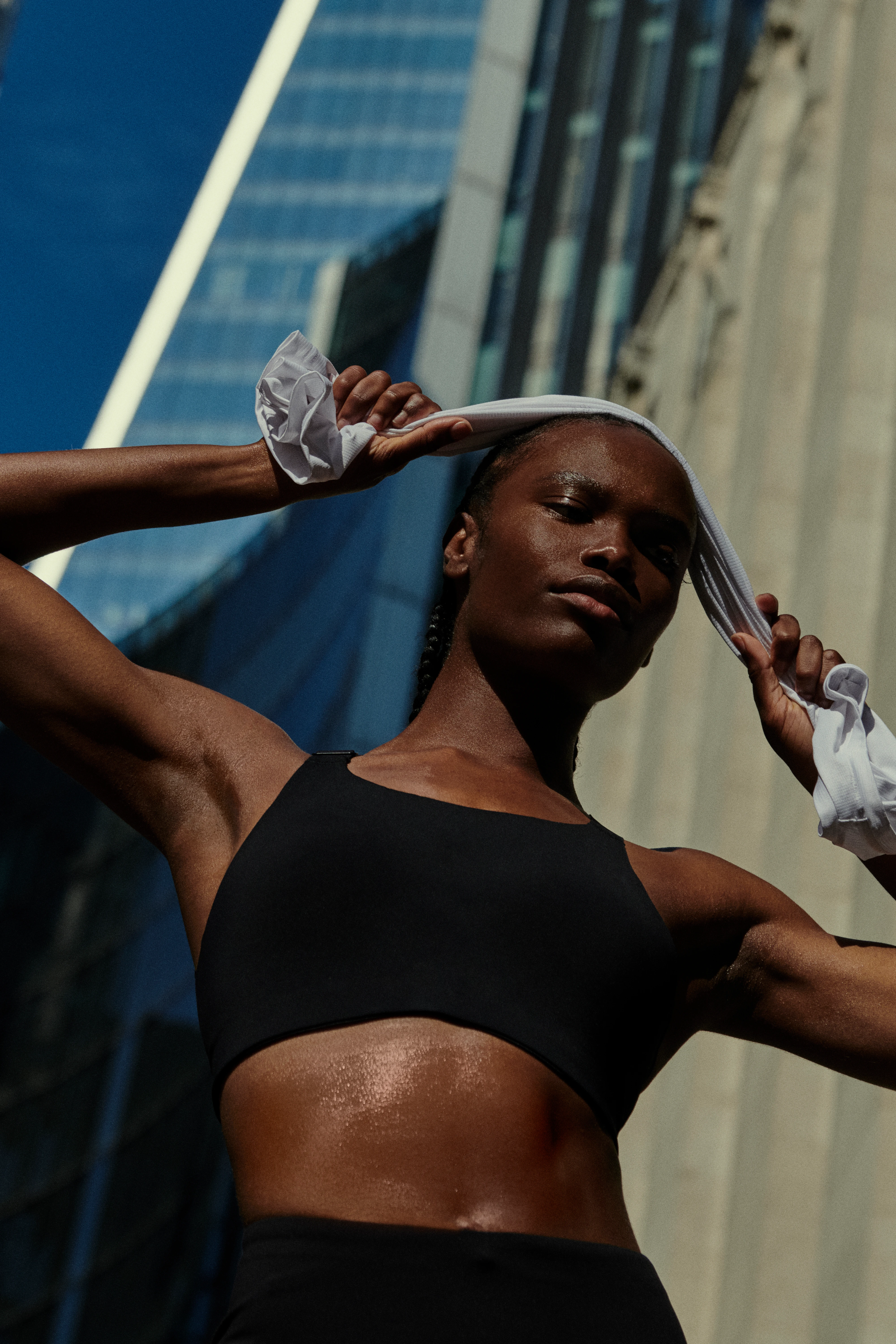Une sportive dehors en brassière noire tient un t-shirt blanc des deux mains au-dessus de la tête après avoir couru.