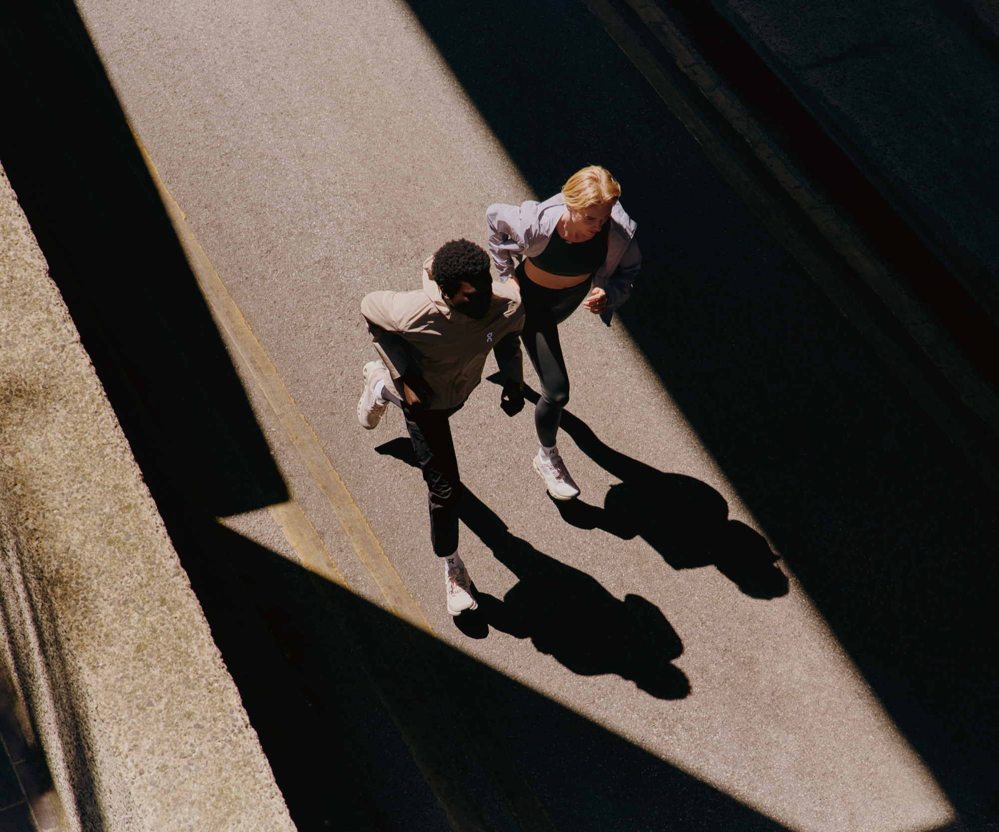 Deux runners dans la rue, portant une veste à capuche et des chaussures de training haute performance On.