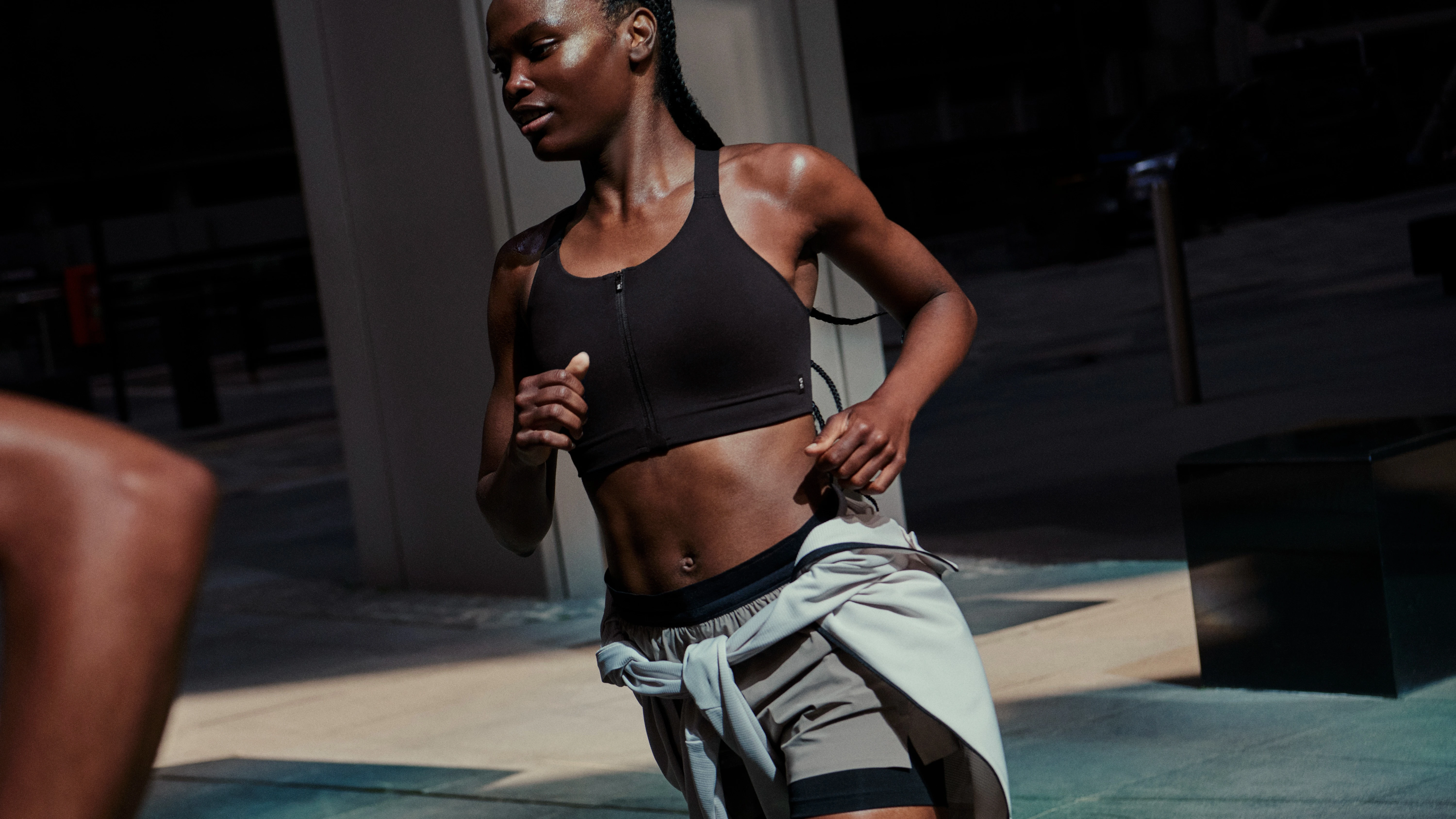 Femme en brassière de sport et short courant en ville, un pull noué à la taille.