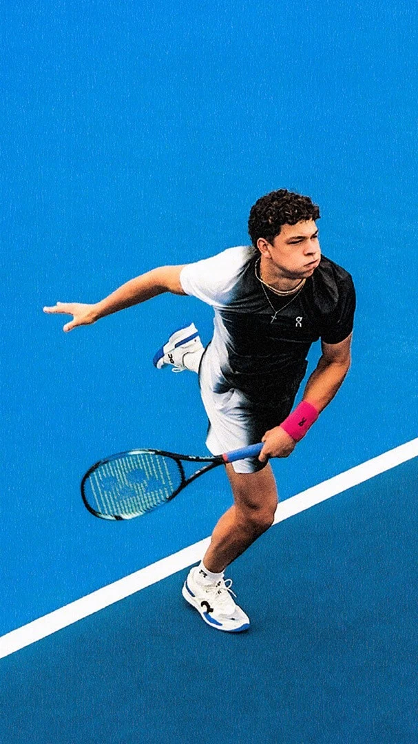 Ben Shelton sur un court de tennis bleu, dans une tenue de tennis On. 