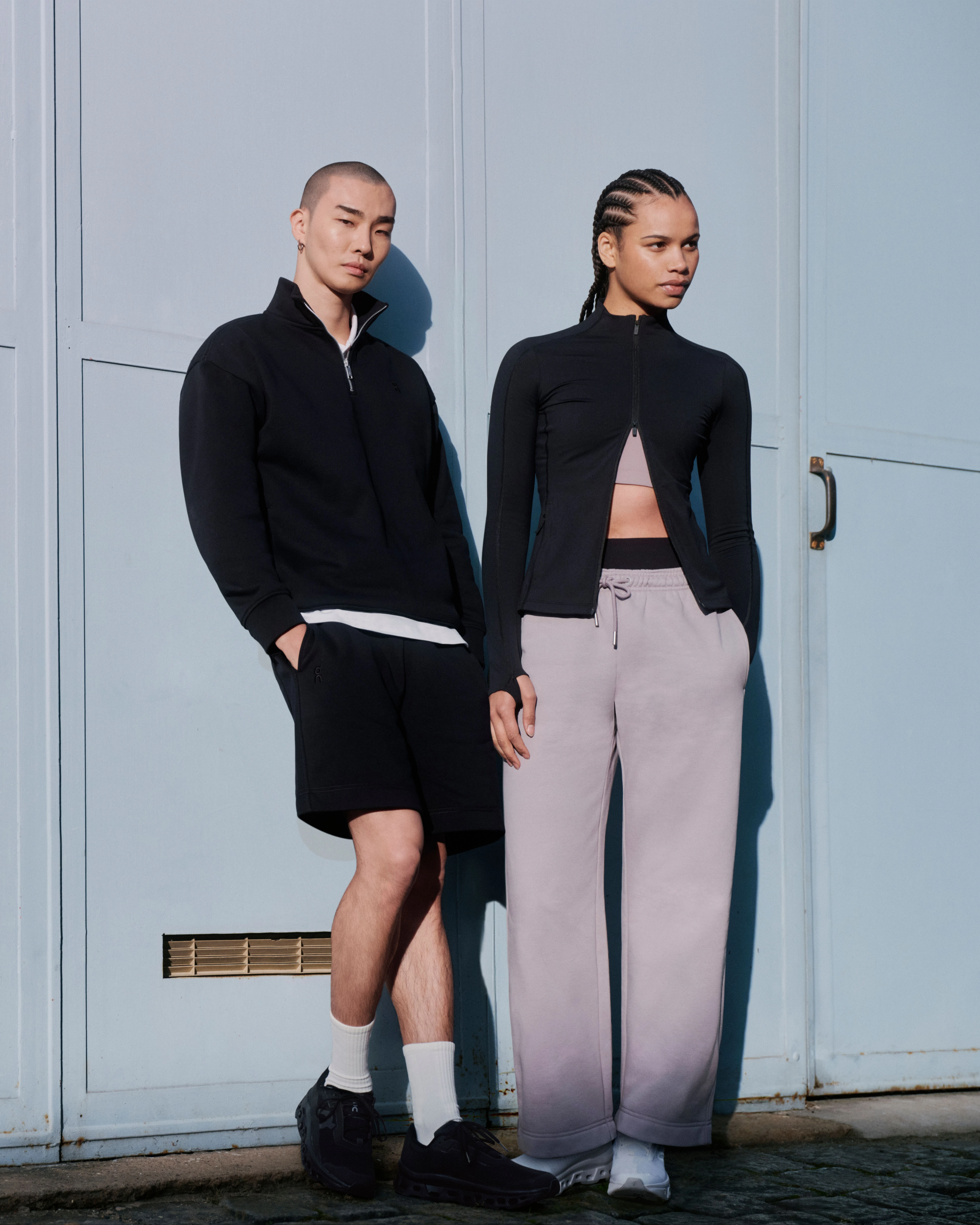 Deux personnes en tenue streetwear On, adossées à un mur.
