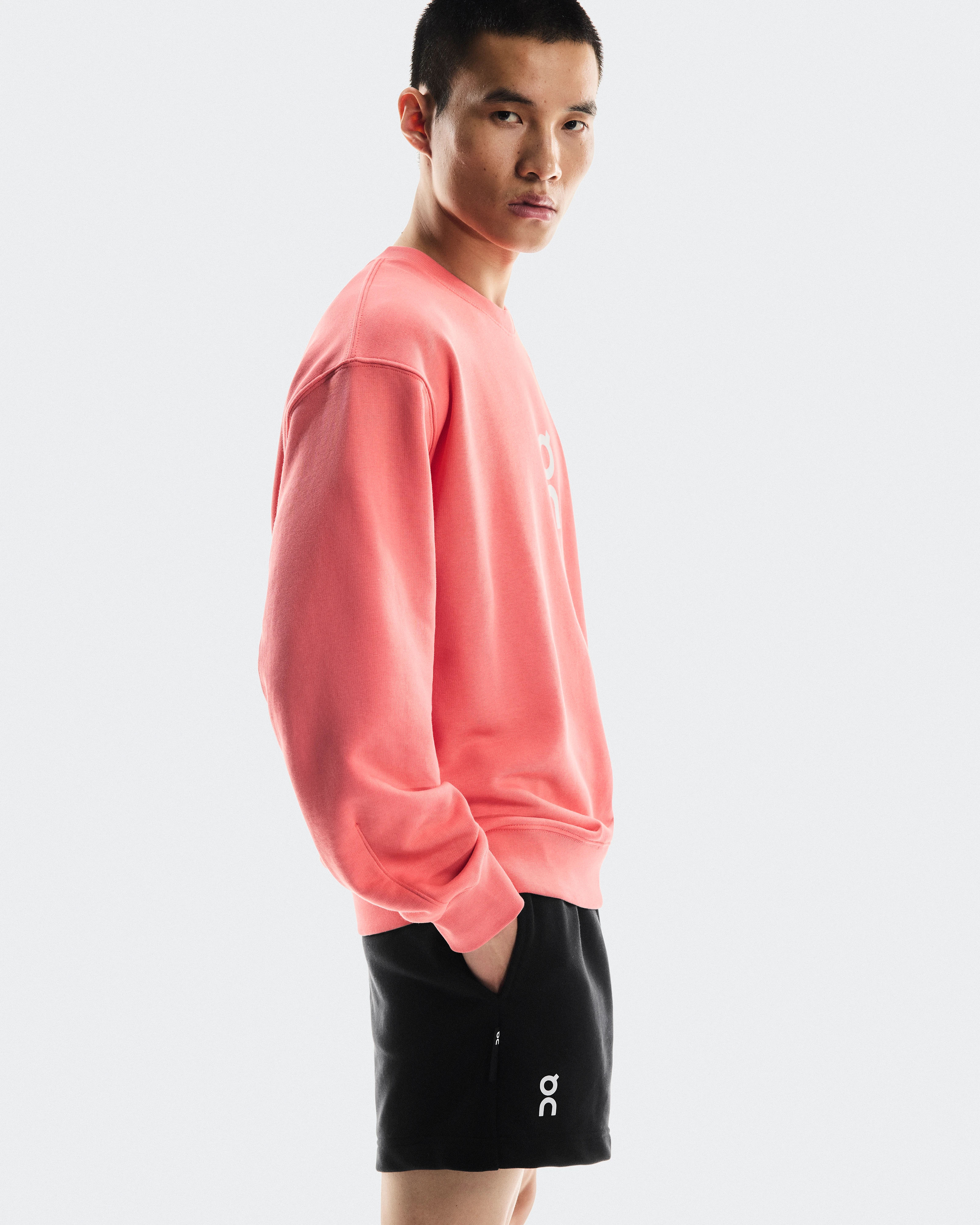 Un athlète au regard sérieux, les mains dans les poches, vêtu d’un short On et d’un sweat-shirt à col rond.