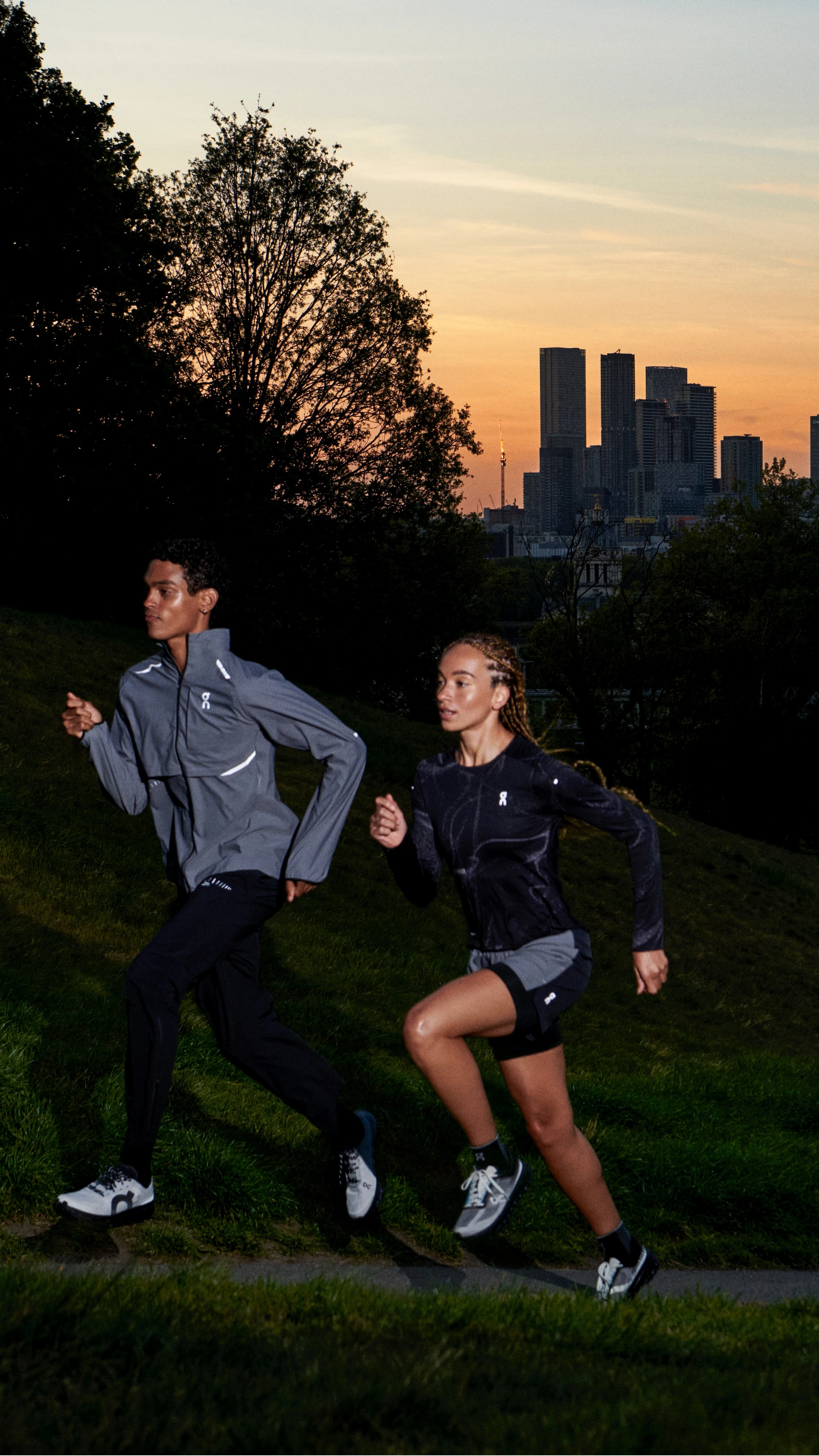 Deux runners courant en montée au lever du soleil avec la ville en arrière-plan.
