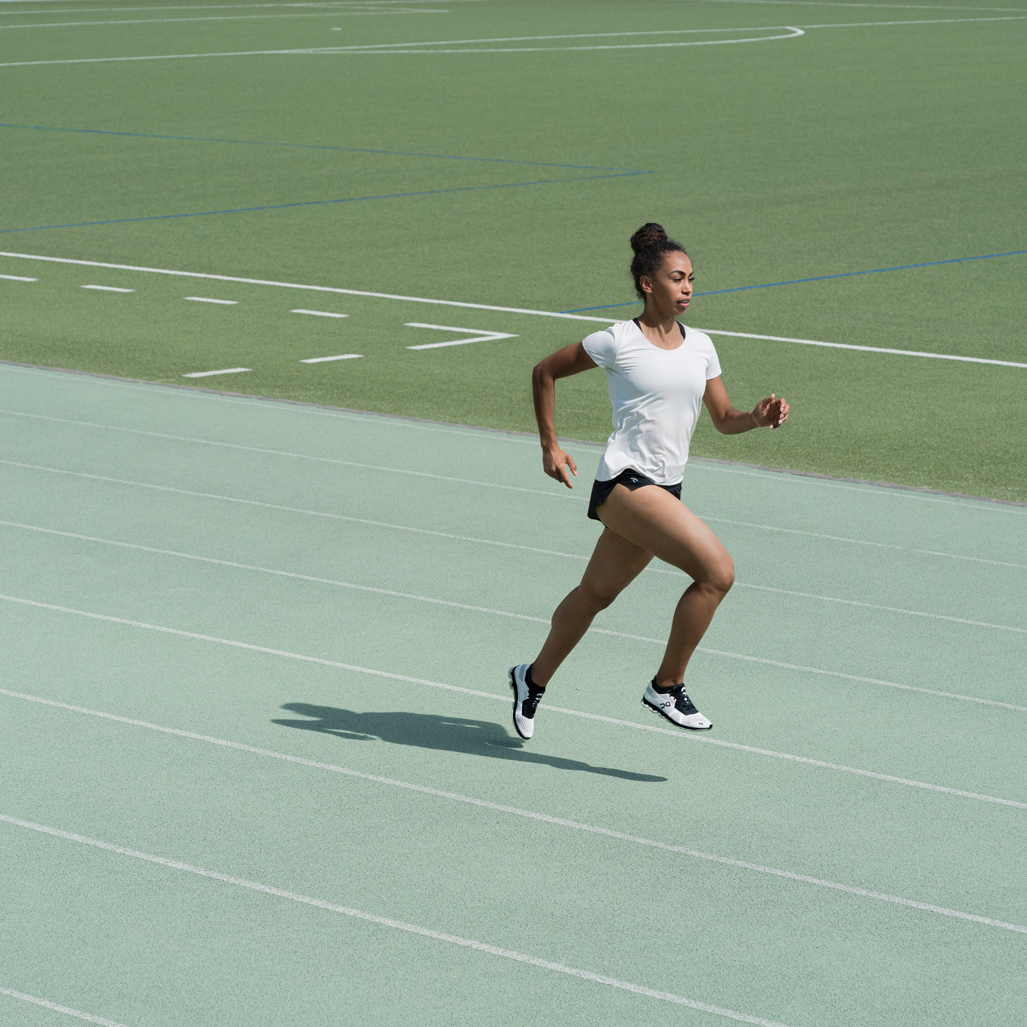 Femme courant sur une piste verte avec un terrain de football en arrière-plan