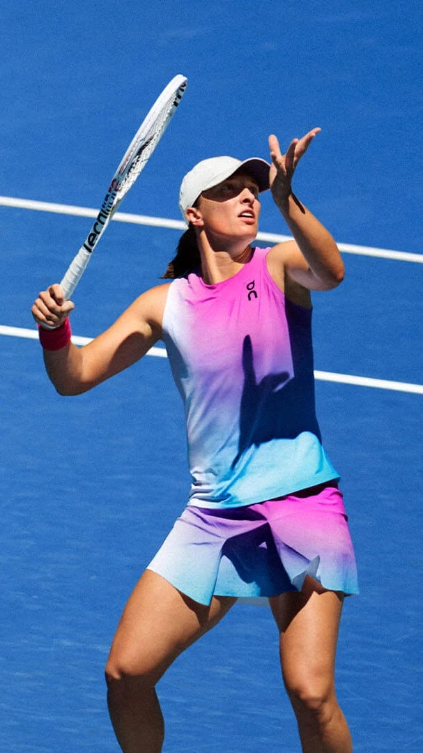 La joueuse de tennis Iga Świątek lance une balle en l’air, vêtue de vêtements multicolores.