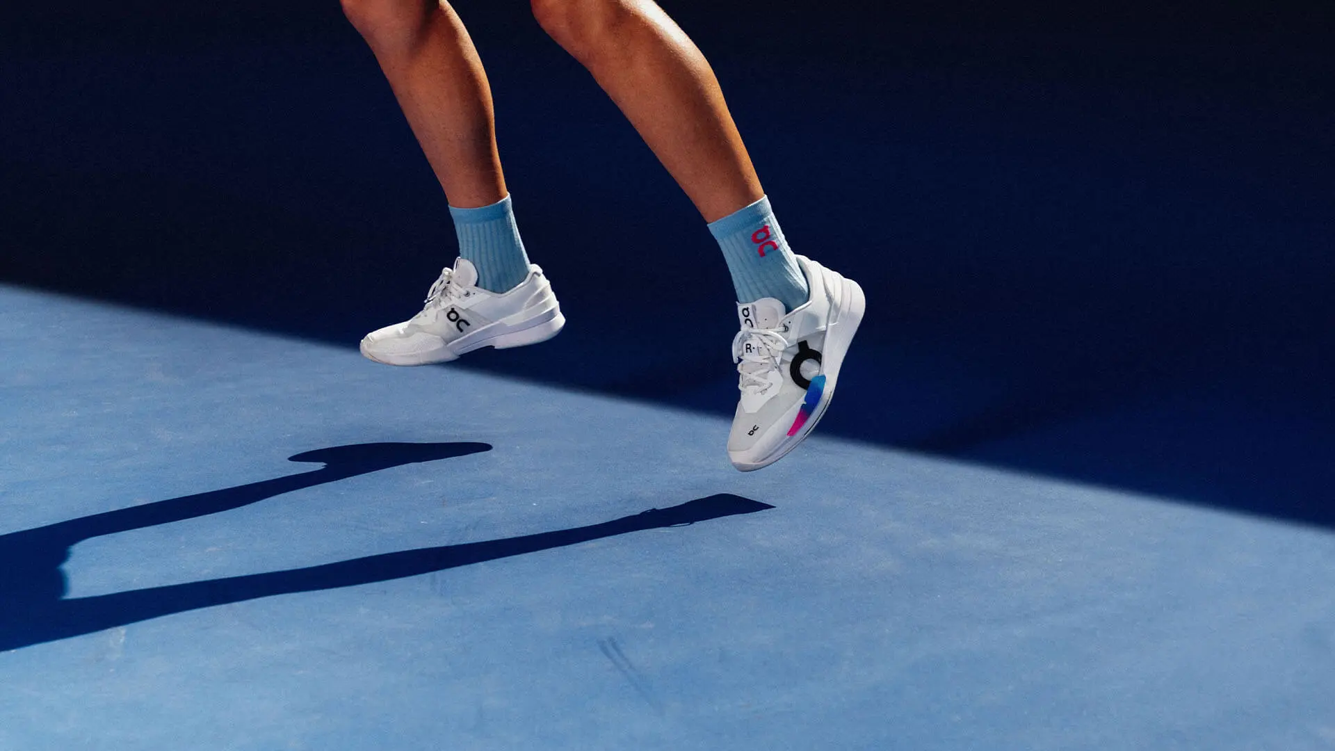 Une personne qui porte des chaussures de tennis et saute sur un court de tennis dur de couleur bleue.